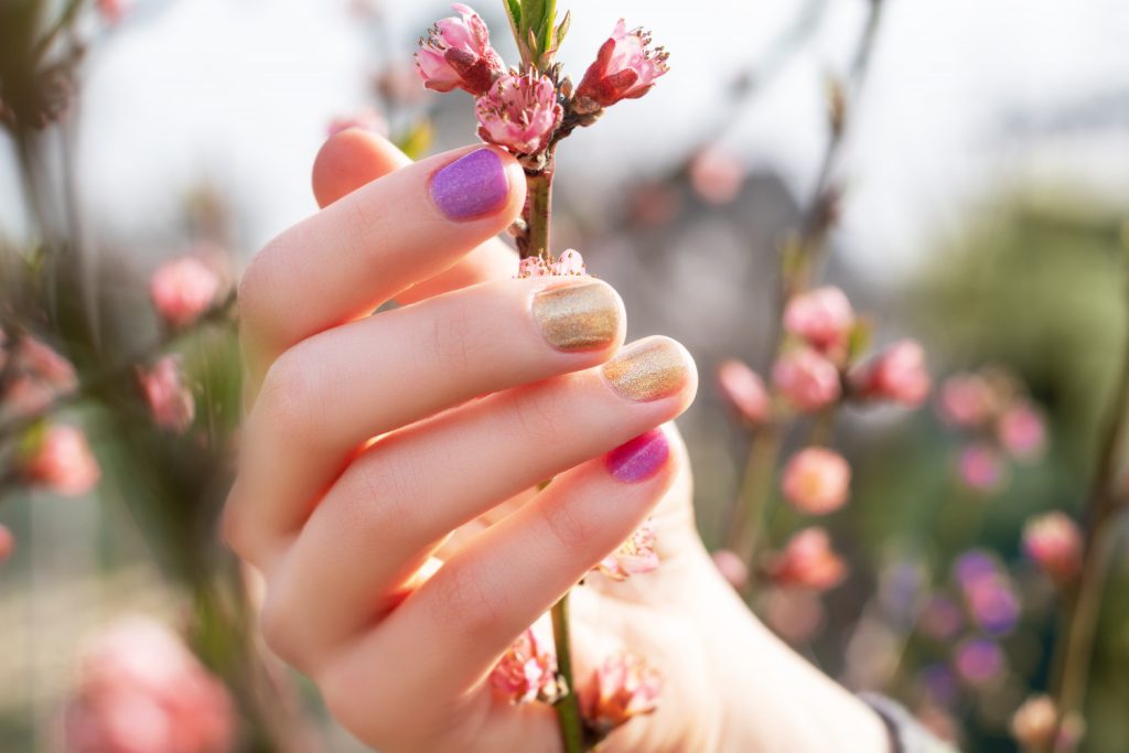 female-hand-with-gold-purple-nail-design-holding-blossom-branch